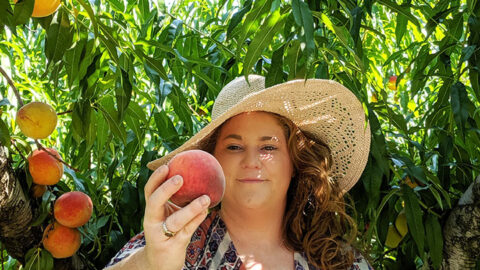Lizzy Chiles holding peaches in front of peach tree at Chiles